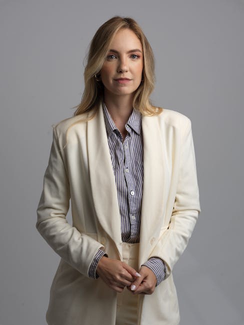 Elegant portrait of a woman in a white blazer with a neutral background, exuding confidence.